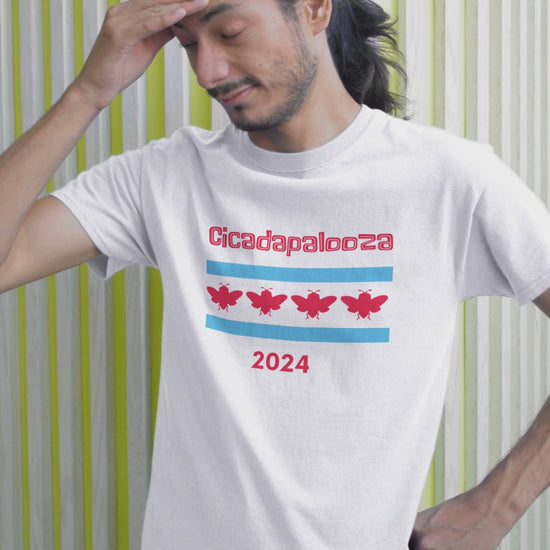 A slim man wears a white t-shirt with "Cicadapalooza" printed on it and the Chicago flag with the red stars replaced by cute, red cicadas. In the video, his face expresses worry and disapproval.