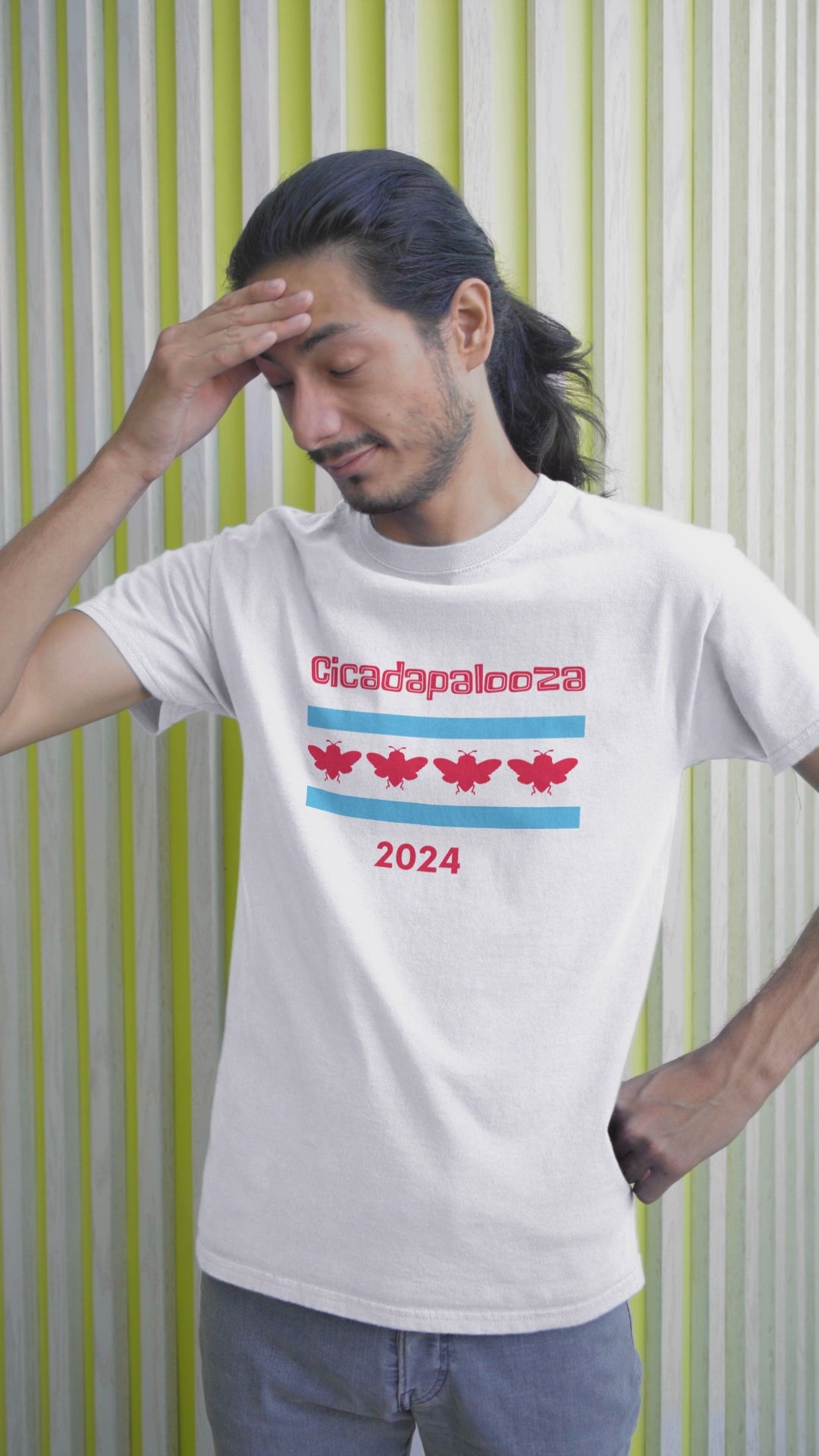 A slim man wears a white t-shirt with "Cicadapalooza" printed on it and the Chicago flag with the red stars replaced by cute, red cicadas. In the video, his face expresses worry and disapproval.